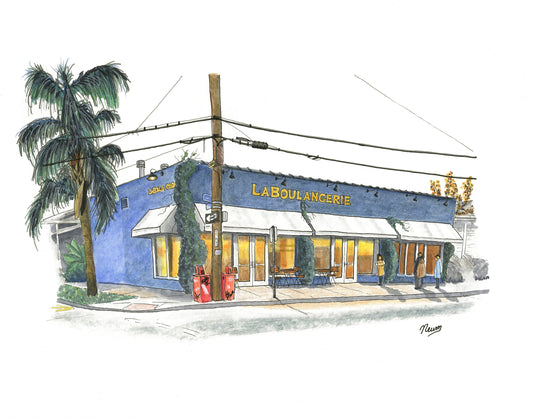 A product photo of the La Boulangerie art print. A navy blue rectangular building is viewed from a corner on Magazine Street in New Orleans. The building houses a the French bakery aptly named La Boulangerie. Vines grow up and down the front of the restaurant. A warm amber glow emanates from the windows while several soon to be patrons wait outside on the sidewalk for the doors to be opened. A palm tree flanks the left and a power pole with newspaper machines sit at its base.